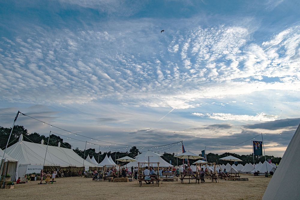 A stunning sunset sky with rippled clouds over the Latitude music festival venue, with luxury camping white tents in the foreground.