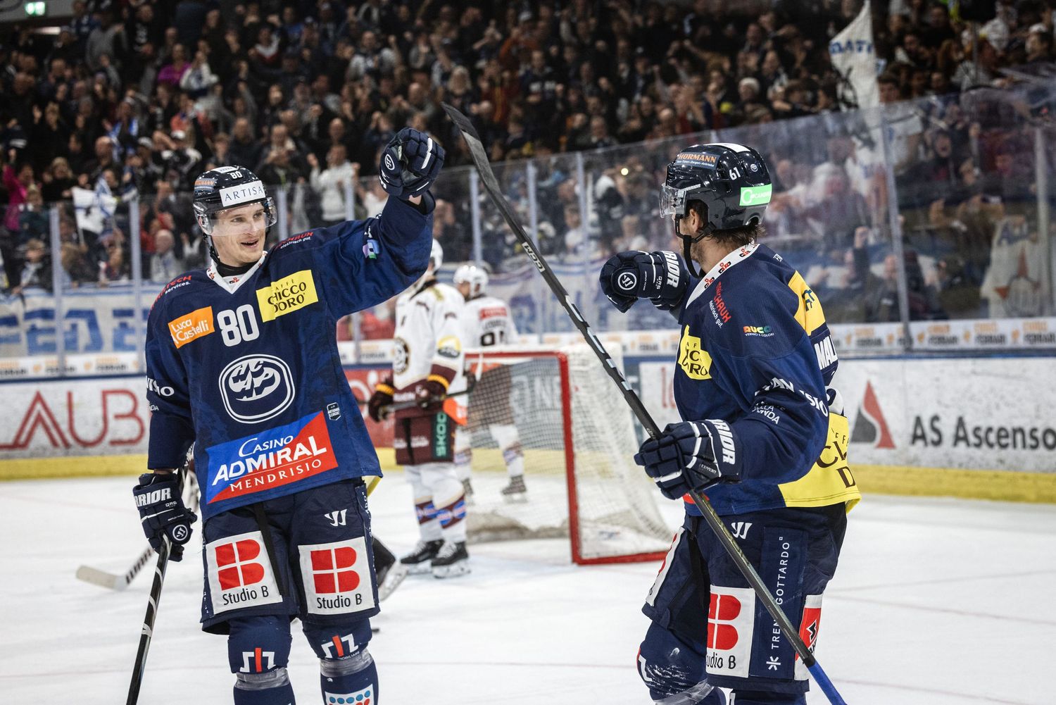 Hockey players celebrate on the ice during a game with a packed crowd watching in the background.