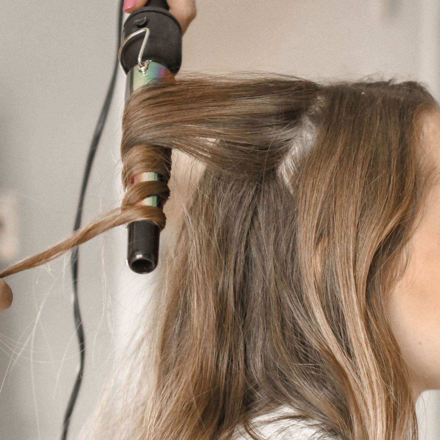 Close-up of styling hair with curling iron showing blonde wavy locks.