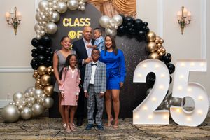 Family of six posing together at a Class of 2025 graduation celebration with black and gold balloon arch.