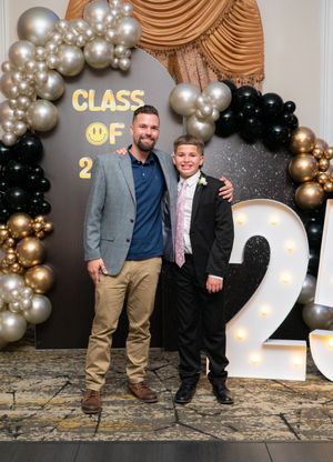 Man and young boy in formal attire smiling together at Class of 2025 graduation celebration backdrop.