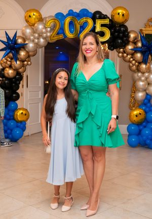 Woman in green dress and girl in blue dress posing under a 2025 balloon arch.