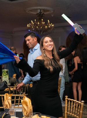 Woman in black dress dancing with light-up foam stick at elegant graduation celebration.