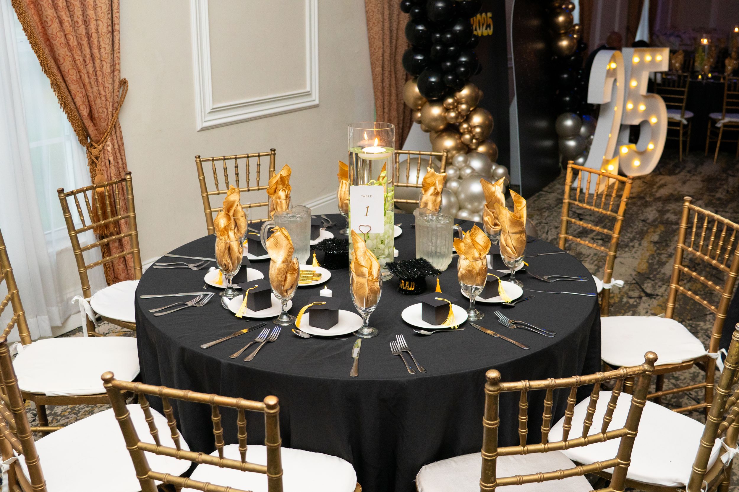 Sophisticated black and gold banquet table setting with floral centerpiece and chiavari chairs.