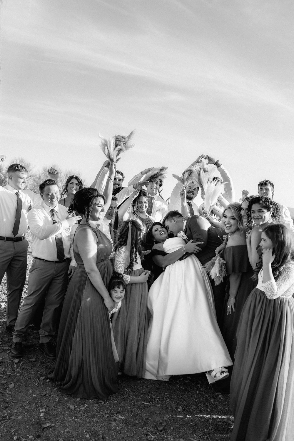 Wedding party celebrates joyfully in black and white photo with bridesmaids in dark dresses.