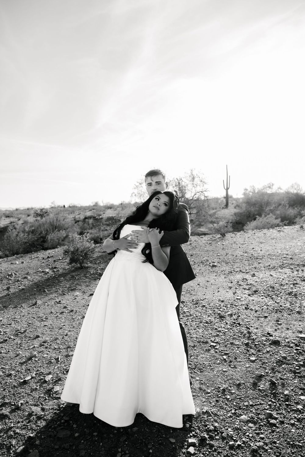 Black and white portrait of couple embracing in desert setting with dramatic composition.