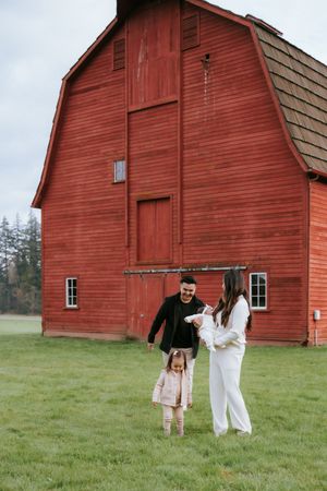 A sequence of five red barn photos in a grassy field showcases a romantic moment between two people in white and black outfits.