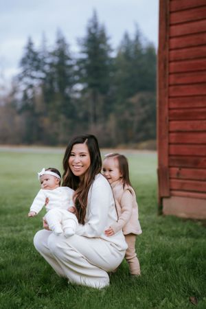 A loving moment outdoors by a red barn as a family spends time together on a green lawn with evergreen trees beyond.