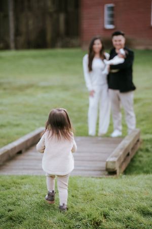A touching family scene by a red barn as a small child walks towards others on a wooden boardwalk.
