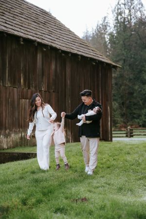 A family with young children spends time together on a grassy lawn in front of a rustic wooden barn.