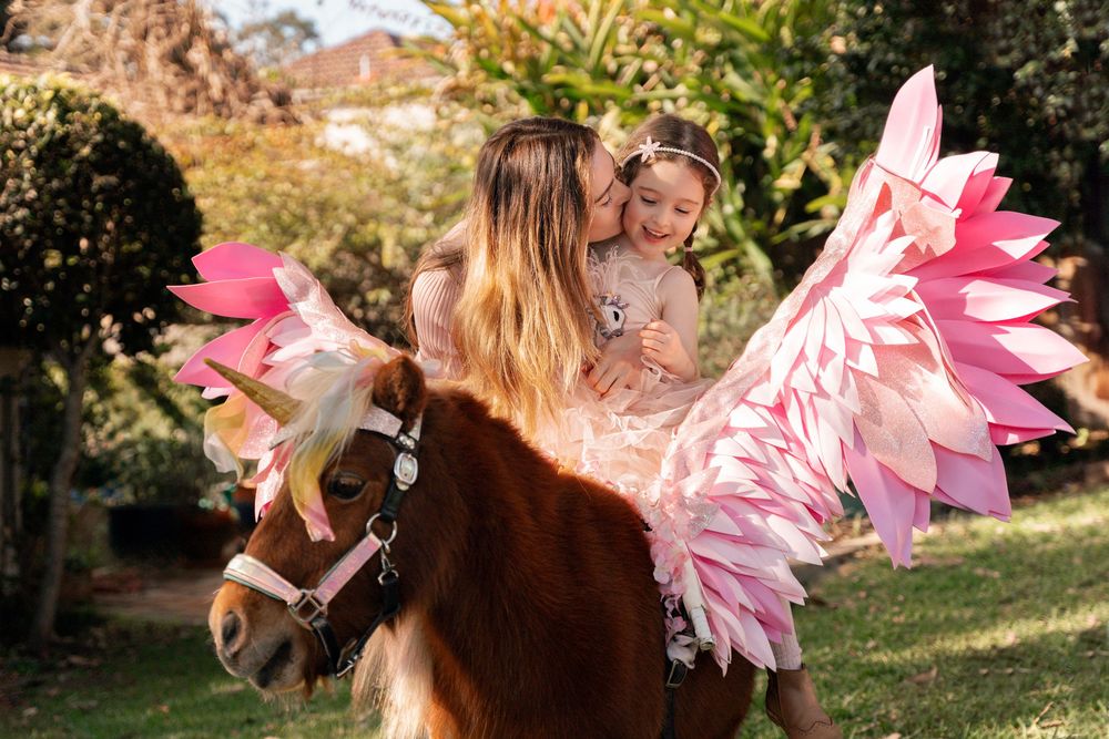 Mom is kissing girl while she is sitting on a unicorn during a unicorn photoshoot in Sydney Lane Cove