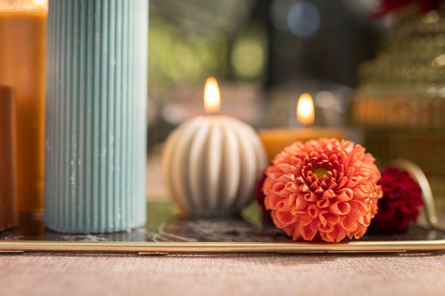 Beautiful orange dahlia flower with candlelit ambiance, featuring a mint green vase and round striped candle in soft focus.