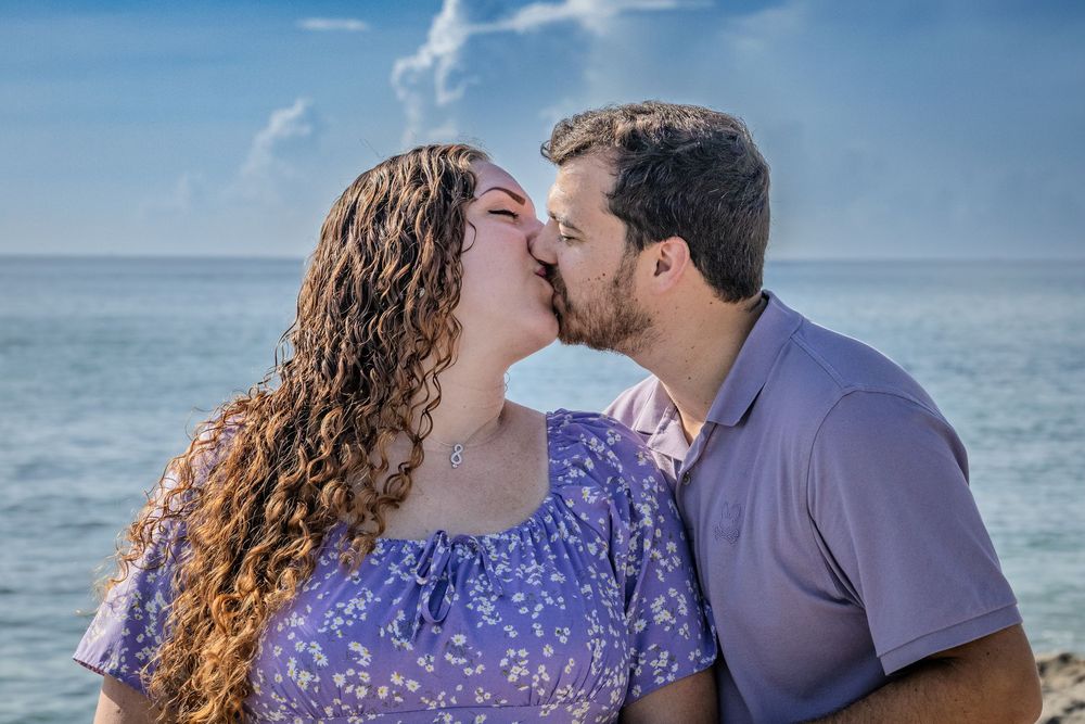 Romantic couple photoshoot at a scenic beach location with waves crashing against rocky shore.