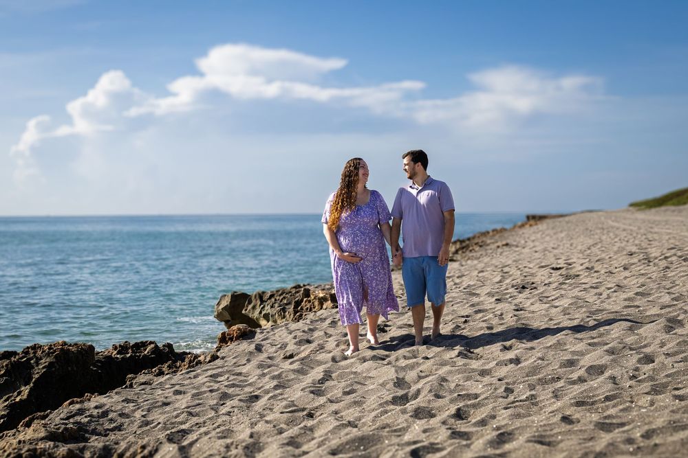 Couple walking dog along scenic beach path during golden hour.