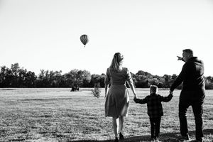 Parents and child walking together toward a hot air balloon floating in the sky