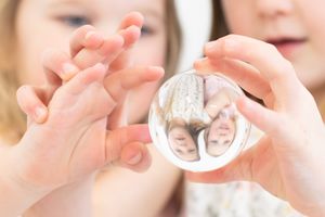 Artistic close-up photo of sisters’ hands playing with a reflection ball