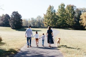 Family holding hands while walking in a park with their dog during an outdoor photo session