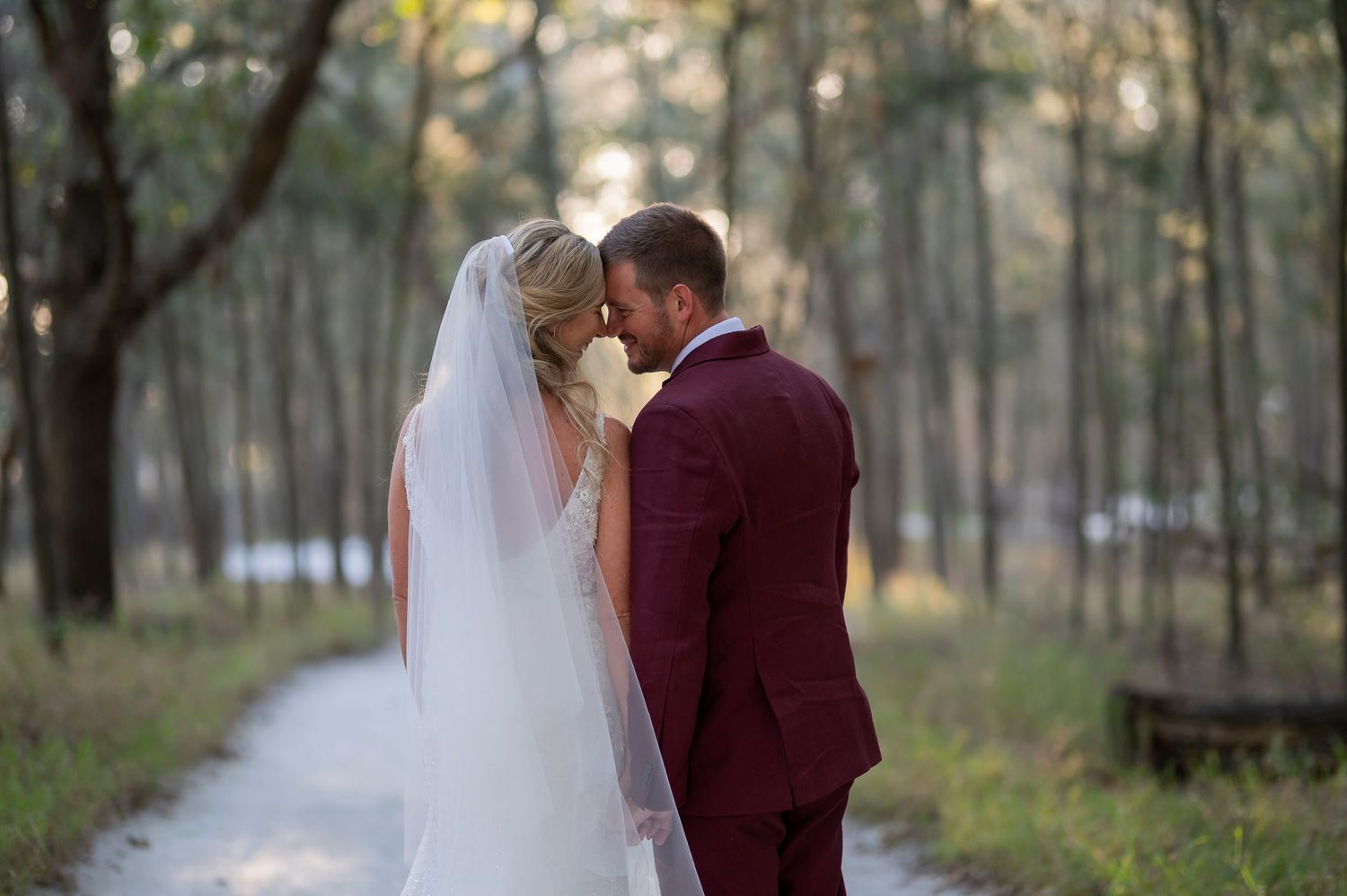 Romantic wedding photo session in a peaceful forest setting with flowing white veil and burgundy suit.