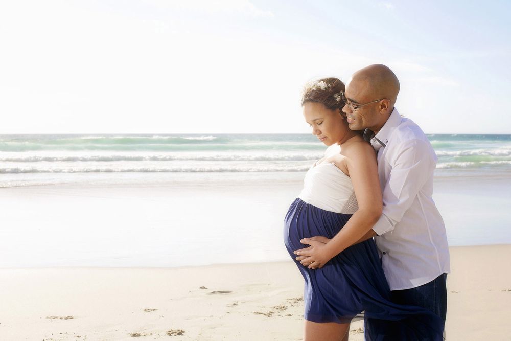 Parents-to-be holding each other in a joyful Melbourne beach maternity shoot