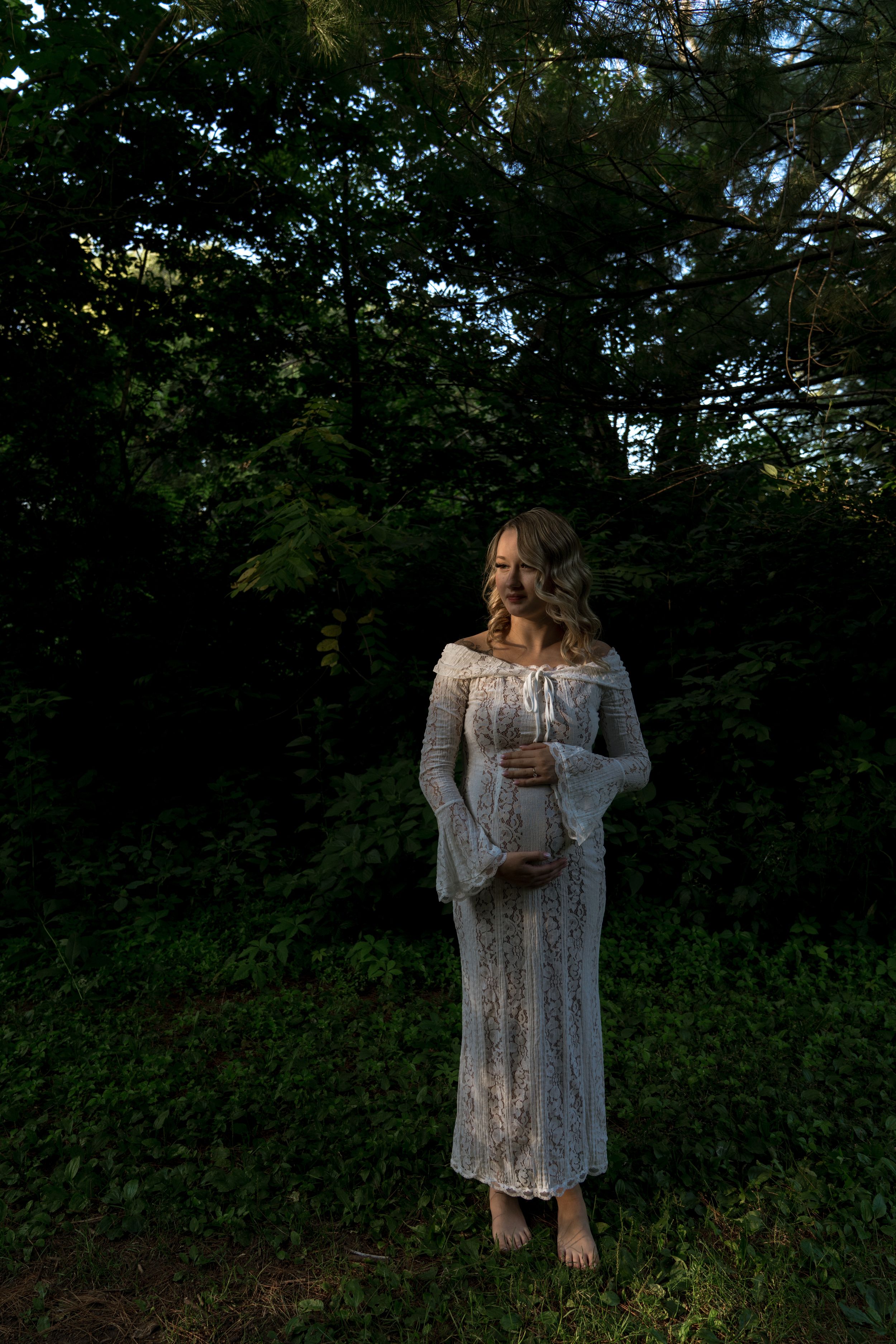 A person in a white lace dress poses against lush green foliage.