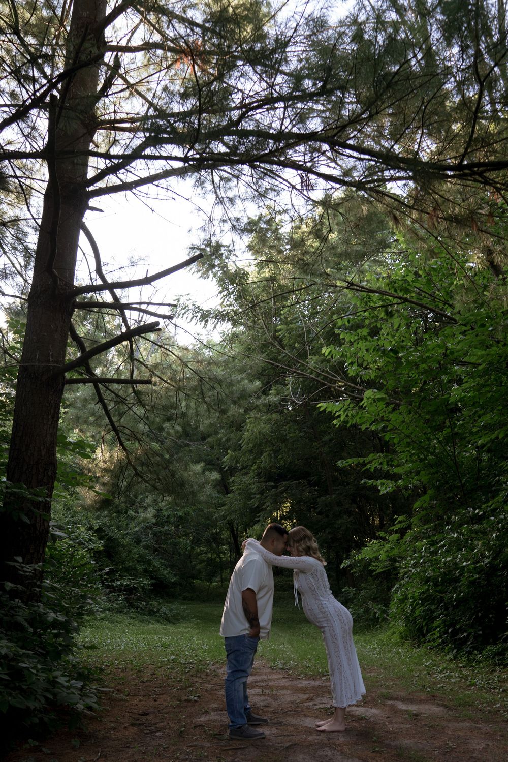 A couple shares a tender moment on a forest path during golden hour.