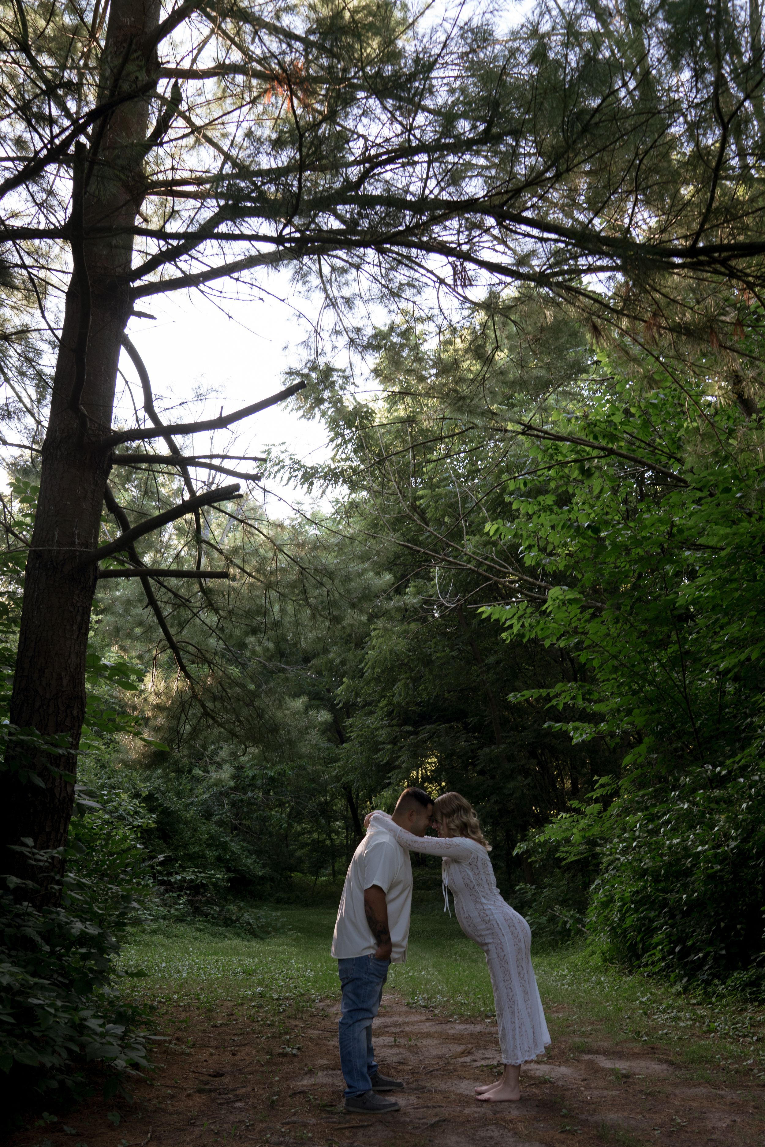 A couple shares a tender moment on a forest path during golden hour.