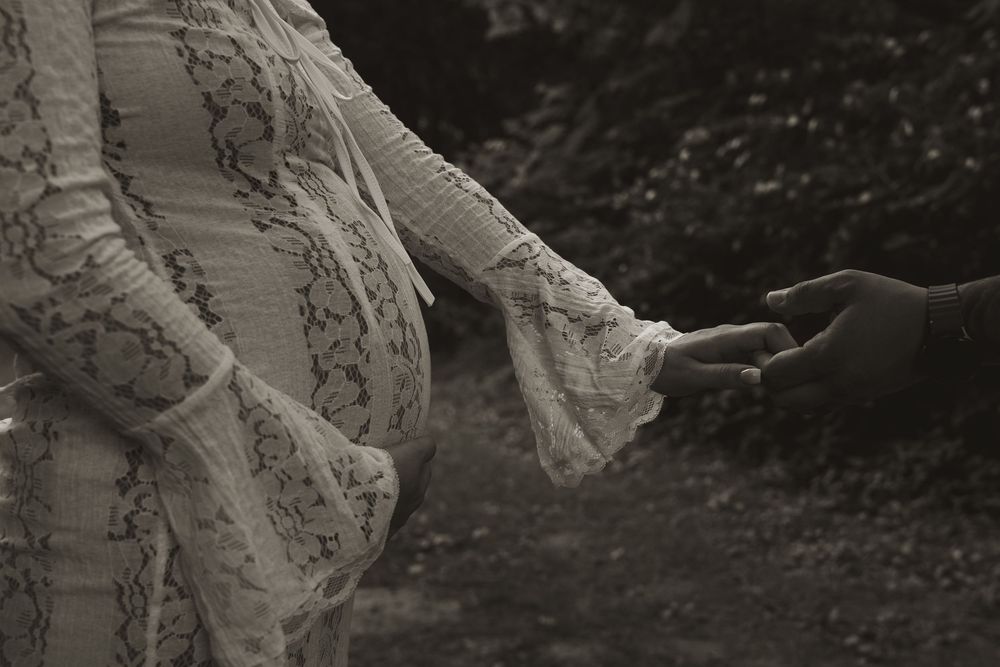 The flowing lace details of a white dress catch the light in a dark forest setting.