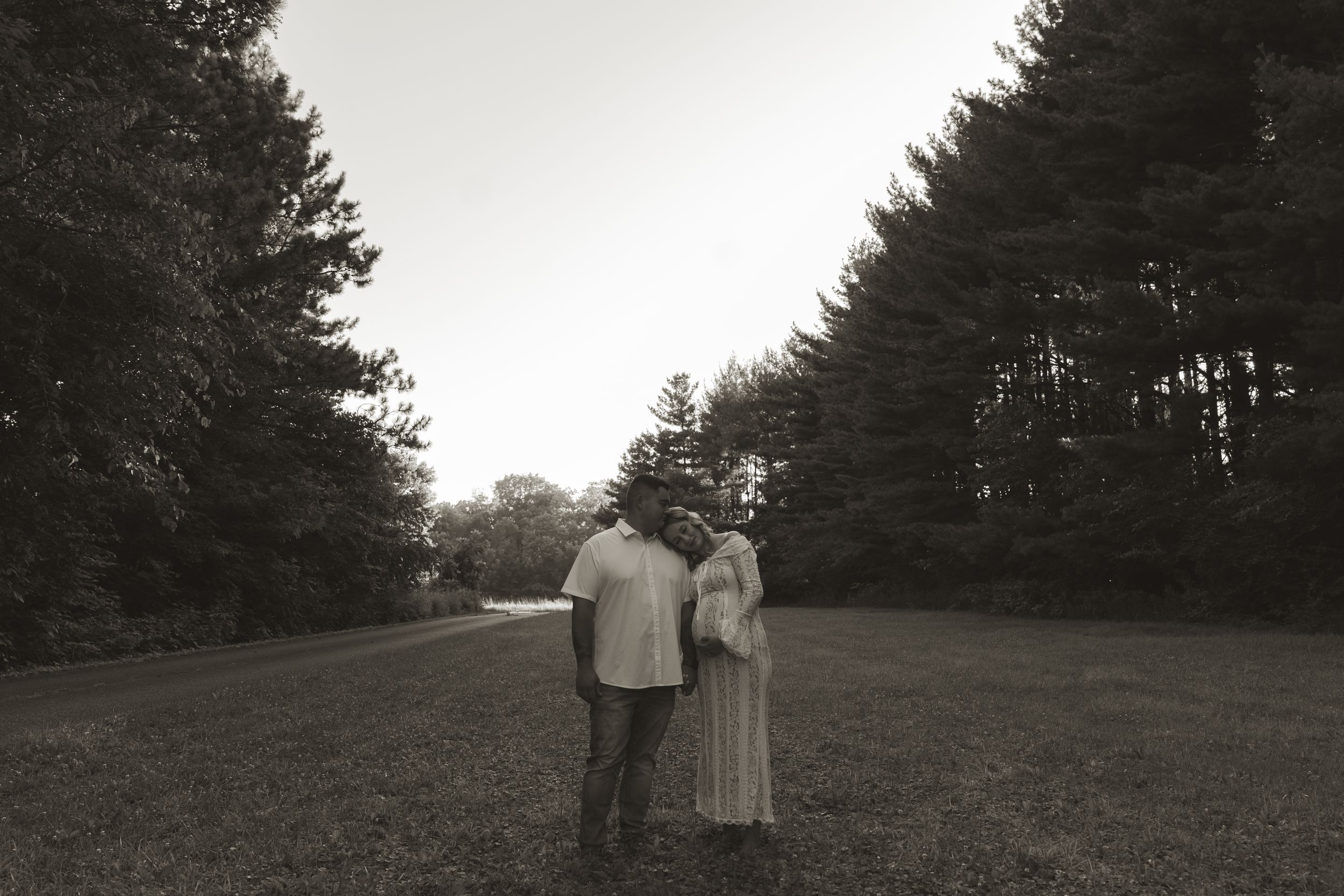 A couple poses together outdoors at dusk with evergreen trees in the background.