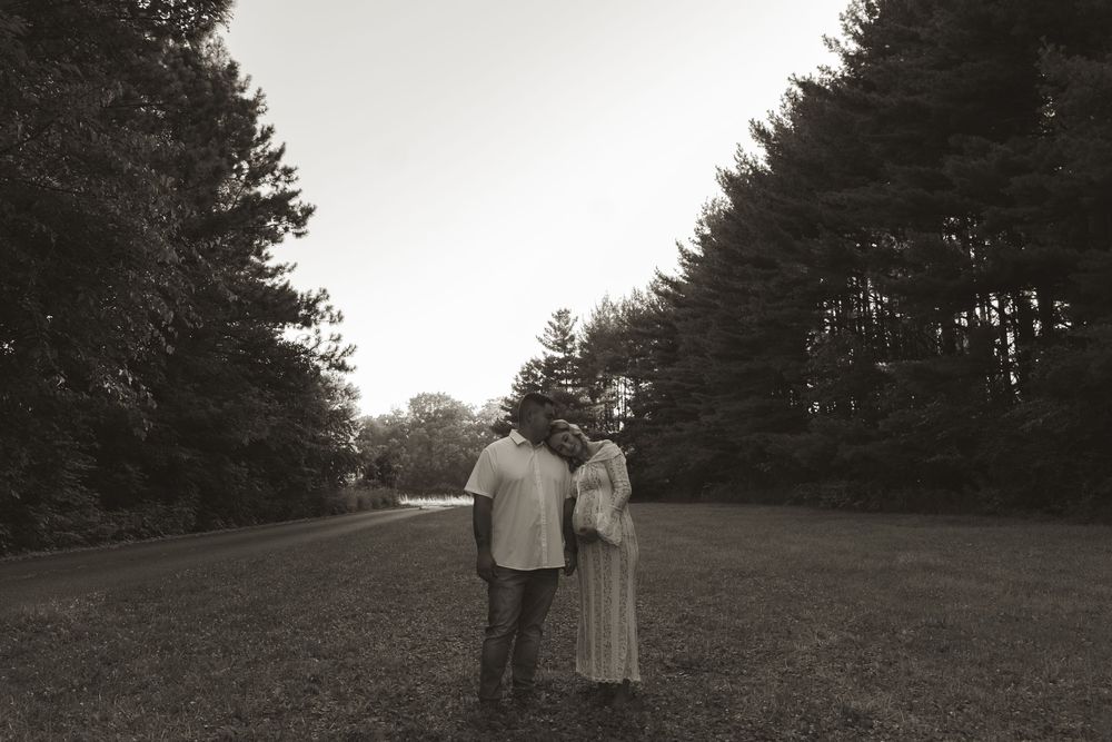A couple poses together outdoors at dusk with evergreen trees in the background.
