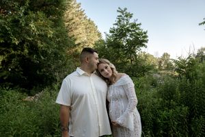 A couple in white outfits embraces in front of lush greenery during golden hour.