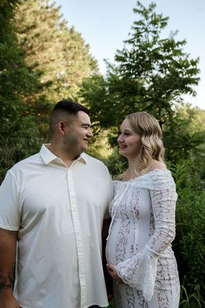 A couple in coordinating white outfits smiles at each other in a garden setting.