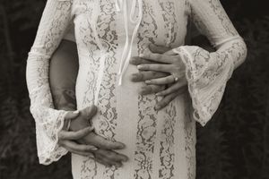 A woman in white lace cradles her baby bump against a dark background.