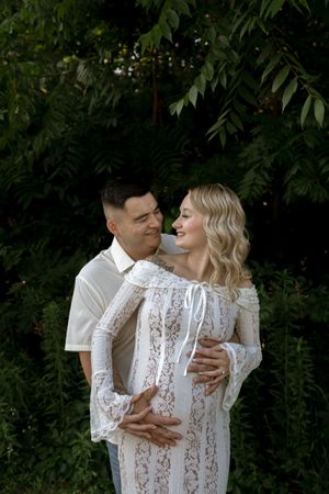 An intimate maternity photoshoot moment captured in a garden setting.