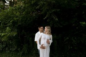A tender moment between a couple in white clothing against a natural backdrop.