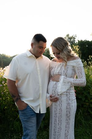 A couple in white clothing poses together during golden hour in a natural setting.