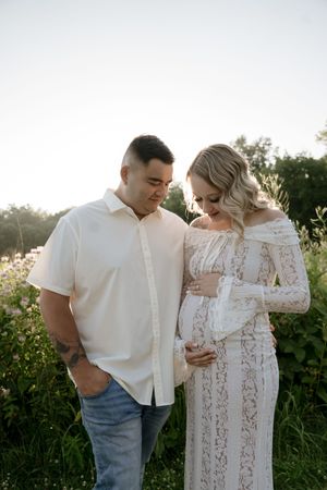 An intimate couples photoshoot in a field during sunset with subjects wearing white.