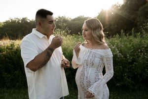 A couple shares a playful moment in a golden-lit meadow during a sunset photoshoot.