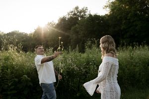 A couple playfully interacts with flowers during their outdoor photoshoot at sunset.