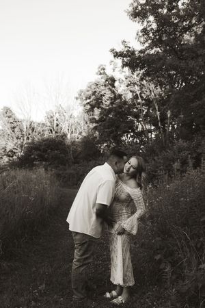 A black and white romantic portrait of a couple in a rustic outdoor setting.