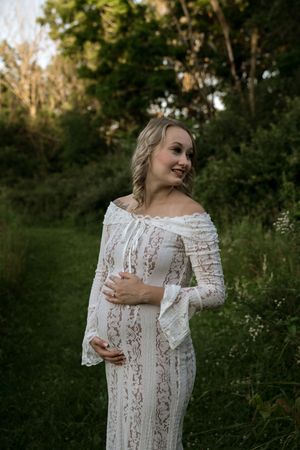 Woman wearing an off-shoulder white lace dress poses in a natural outdoor setting.