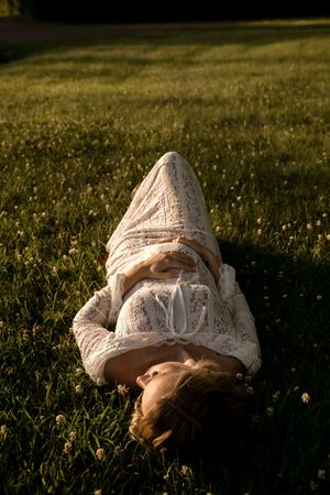 Woman in white lace dress lying in grass during golden hour photography session.