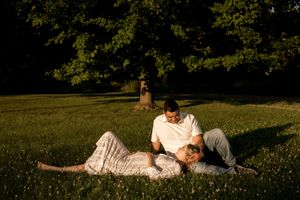Couple relaxes together on grass during outdoor maternity photoshoot.