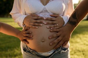 Close-up of pregnant belly with hands gently placed on top during outdoor photoshoot.