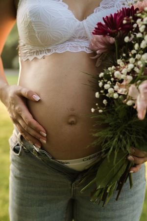 Maternity photo showing pregnant belly with white lace bra and flowers.