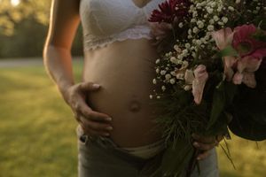 Close-up maternity photo of pregnant belly with floral bouquet against sunset light.