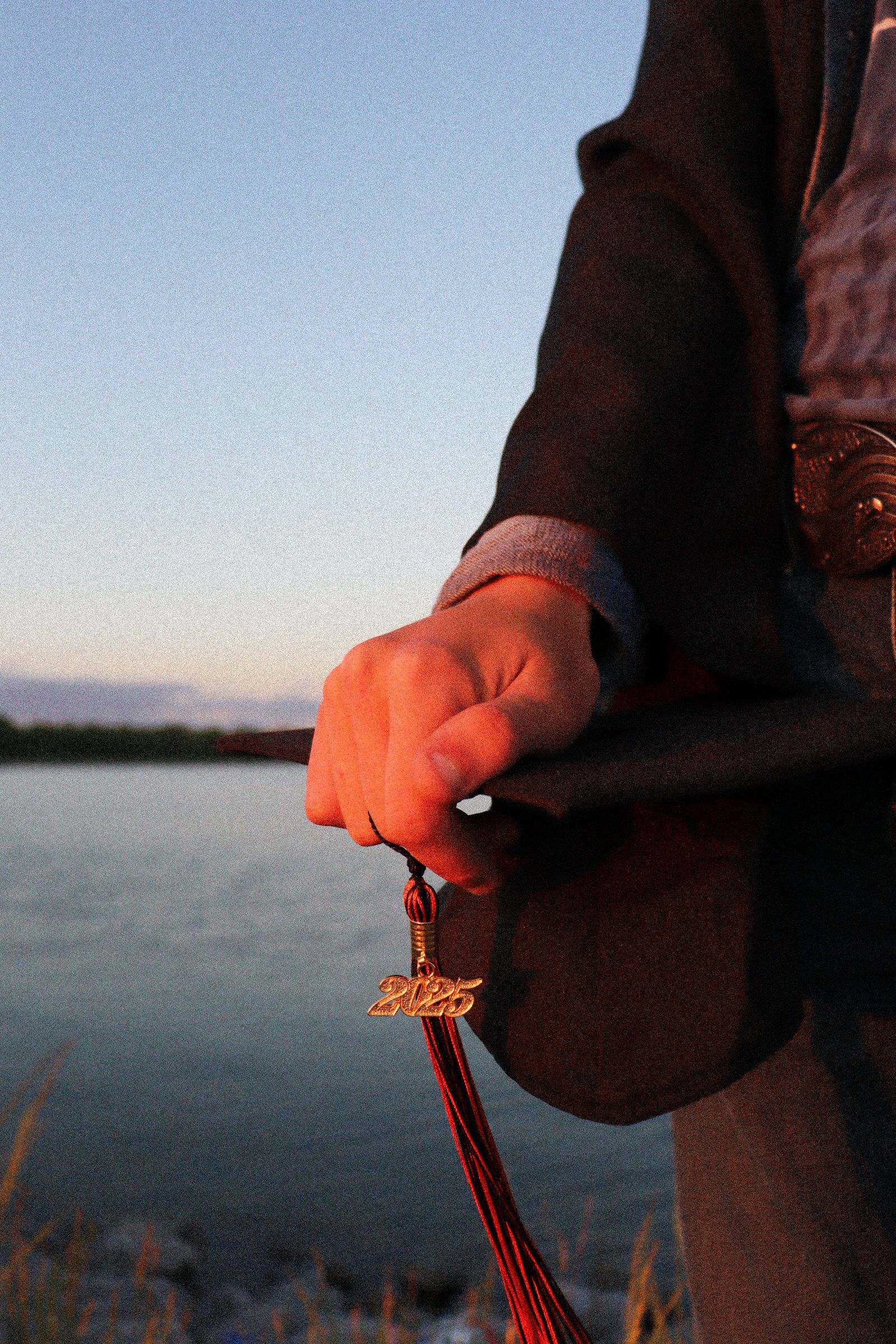 A hand holding leather reins against a tranquil lake backdrop at sunset with warm golden lighting.