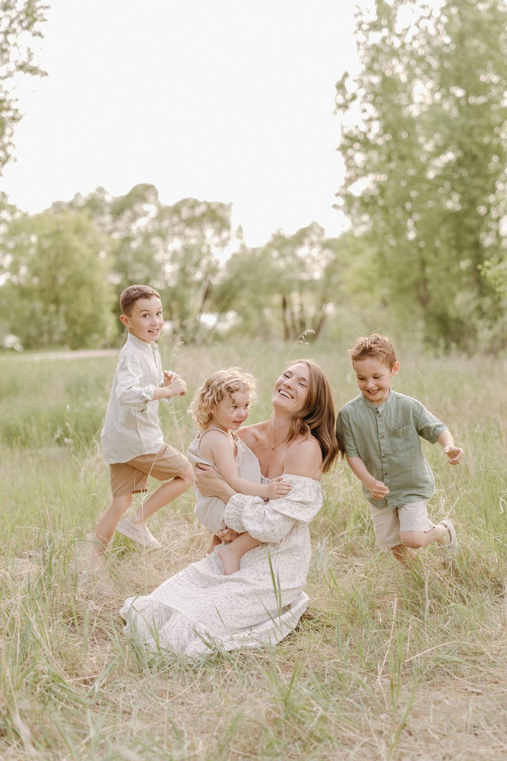 A joyful outdoor family moment in a sunlit meadow with tall grass and trees in the background.
