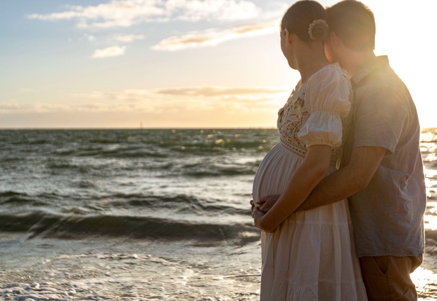 A silhouette of a couple embracing at sunset by the ocean waves.