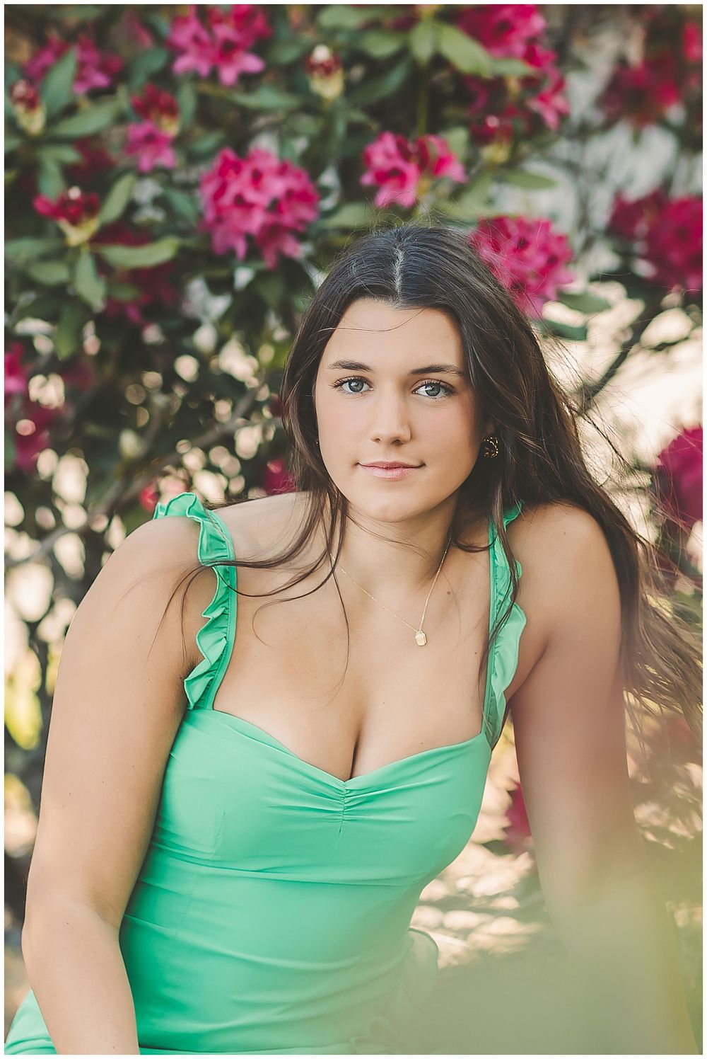 Portrait against vibrant pink flowering bush wearing mint green ruffle strap top in garden setting.