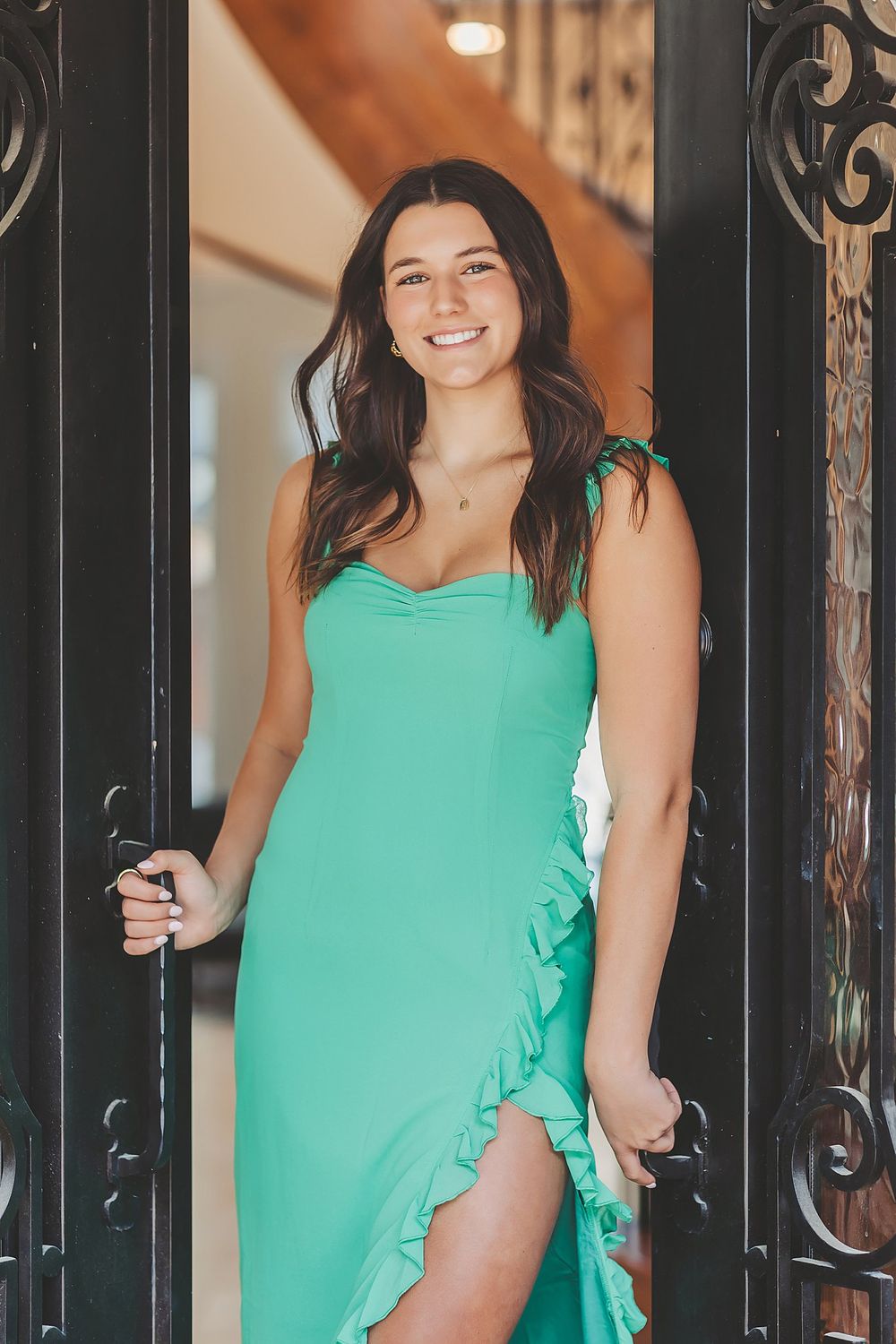 A woman in a mint green dress with ruffles stands in an ornate doorway.